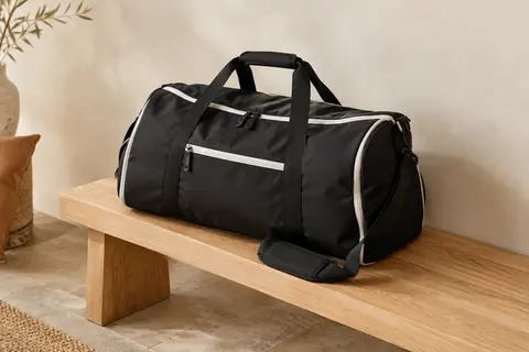 Sac de voyage souple noir aux détails blancs, posé sur un banc en bois dans un décor clair et naturel.
