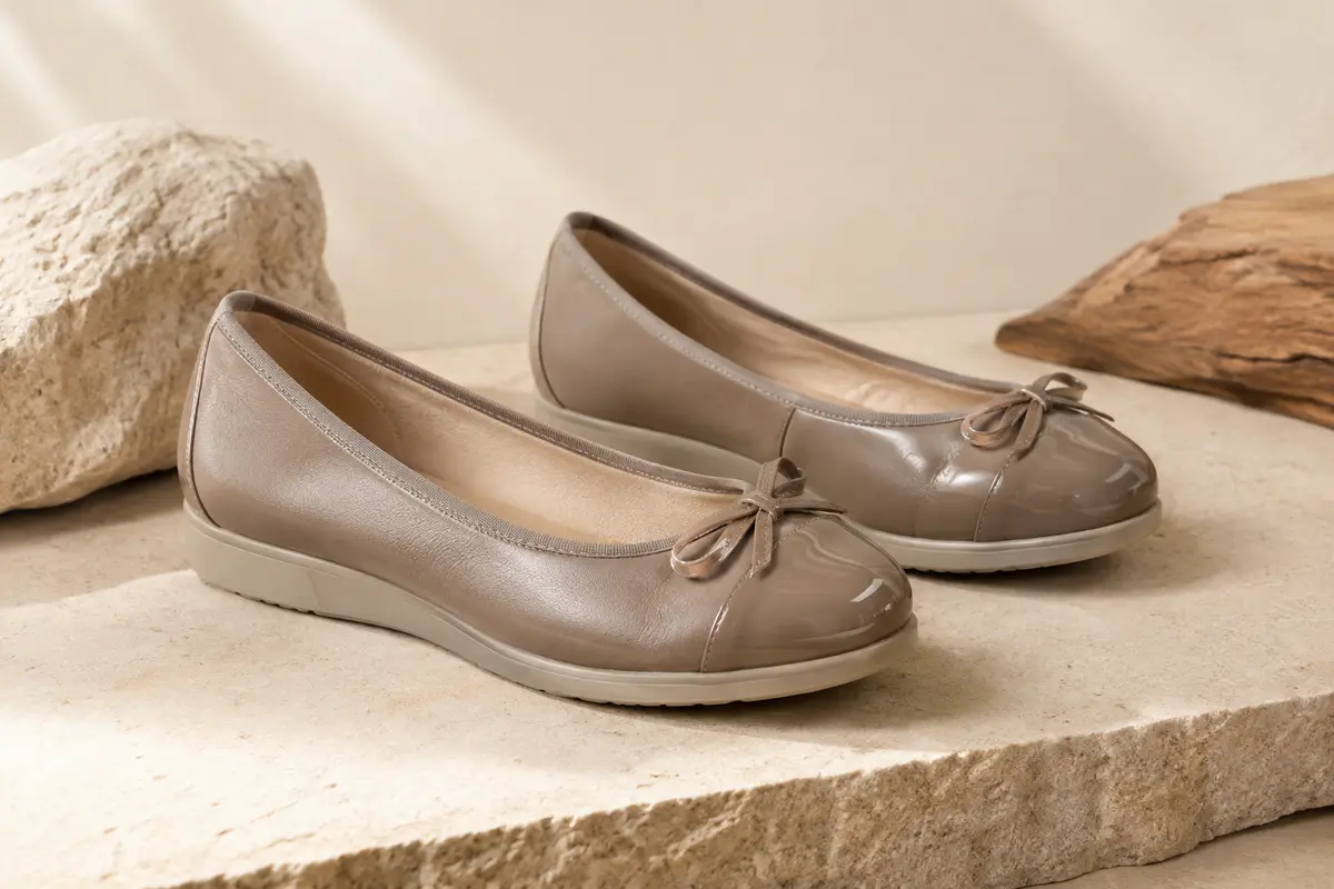 Ballerines fille en cuir avec détails vernis, présentées sur une pierre mate dans une lumière naturelle douce.
