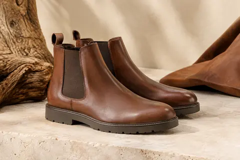 Bottines Chelsea pour homme en cuir à tige courte et semelle en caoutchouc, présentées sur une pierre claire.