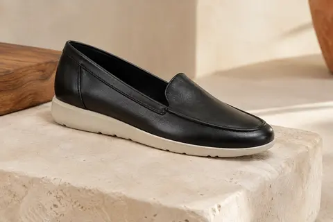 Mocassin Clarks Sharon Gracie noir en cuir présenté sur une pierre claire dans une lumière douce.