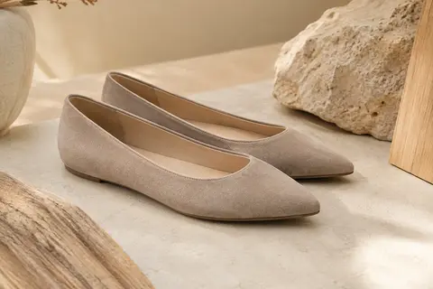 Paire de ballerines à bout pointu en faux suède présentée sur un fond ivoire et sable