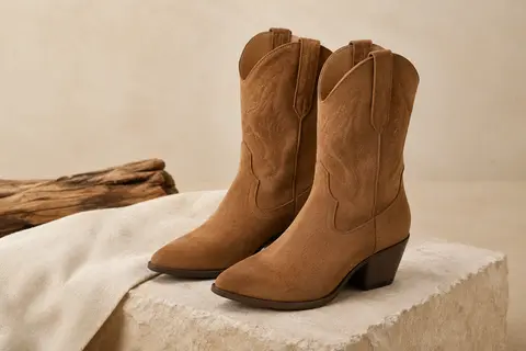 Bottes Elara au style western en matière synthétique, présentées sur un fond sable avec une pierre mate.