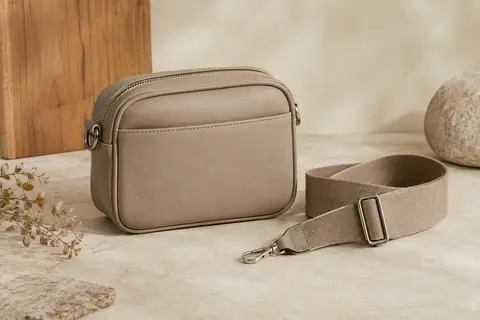 Petit sac bandoulière structuré en cuir PU avec large sangle réglable, posé sur un fond sable.