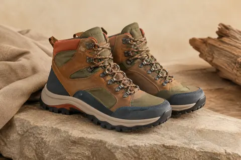 Paire de chaussures de randonnée montantes en simili cuir multicolore posée sur une pierre mate