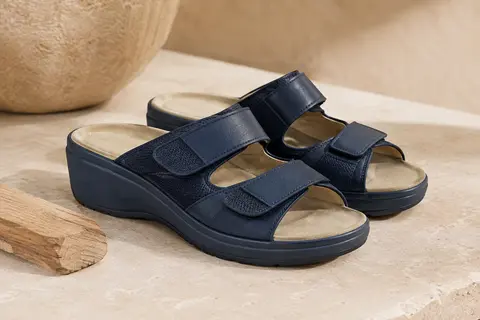 Paire de mules Rieker bleues à fermetures autoagrippantes, posées sur une surface minérale claire.