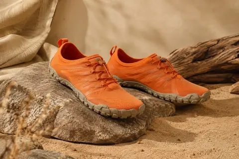 Chaussures minimalistes de trail orange avec semelle en caoutchouc, présentées sur une pierre mate.